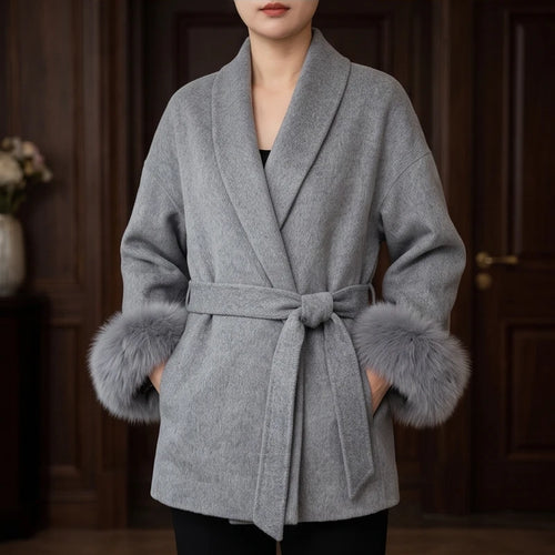 Woman wearing a gray wool coat with a wide lapel, tied waist, and luxurious gray fur cuffs.
