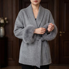 Woman wearing a luxurious gray wool wrap coat with wide lapels and thick gray faux fur cuffs, tied at the waist.