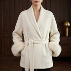 Woman wearing a cream wrap coat with a wide lapel collar, tied belt, and fluffy faux fur cuffs.