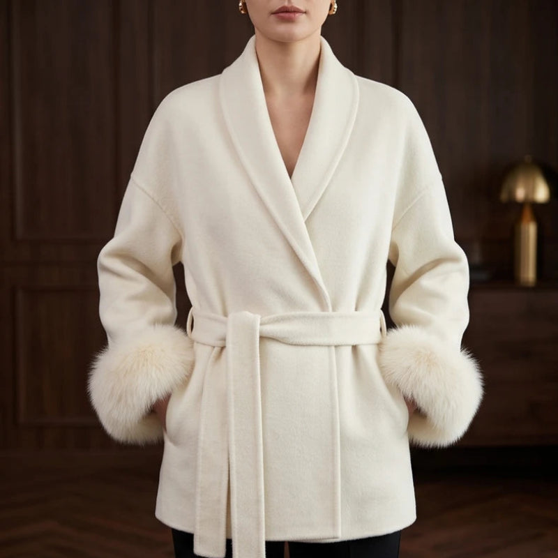 Woman wearing a cream wrap coat with a wide lapel collar, tied belt, and fluffy faux fur cuffs.