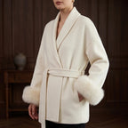 Woman wearing an ivory wrap coat with a wide collar, belted waist, and plush light brown fur cuffs.